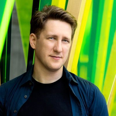 Conductor Joshua Weilerstein standing in front of a vibrant green background